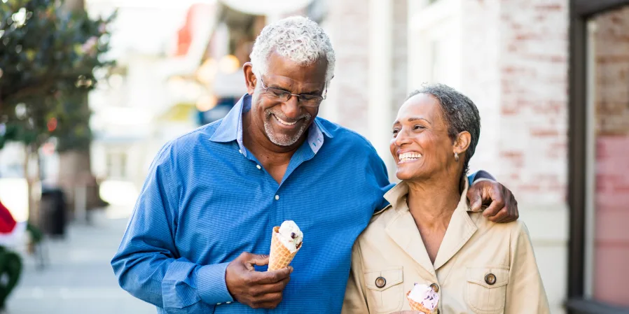 Senior couple walking on sidewalk eating ice cream and smiling