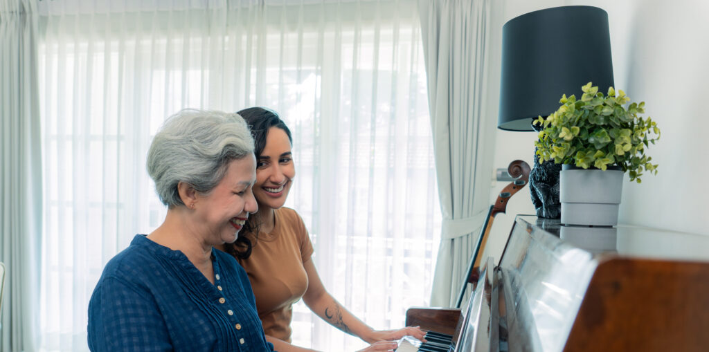 A mixed-race mid-adult daughter joyfully playing piano with her healthy and cheerful Asian senior retired mother on the weekend.