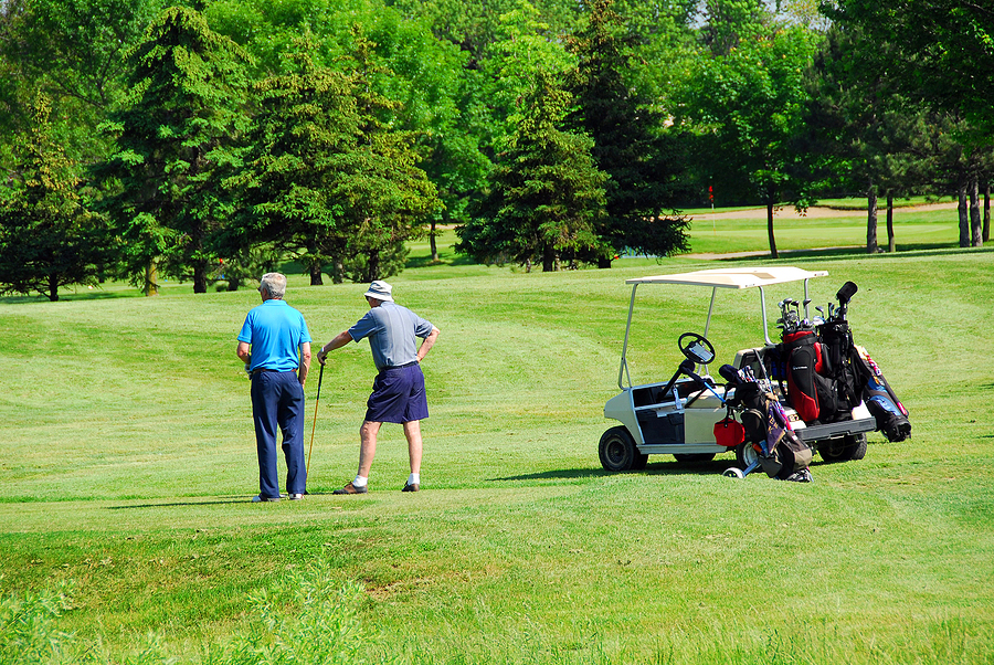A vibrant outdoor photograph of two senior male golfers measuring up a putt.