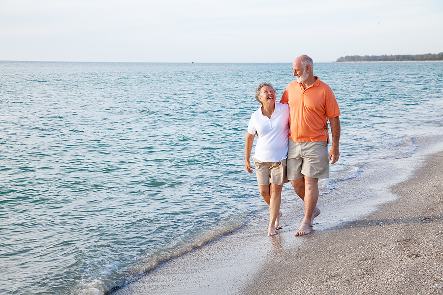 A senior couple enjoys a stroll on the beach together.